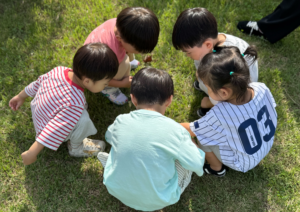 Group of young students in a circle looking at the grass