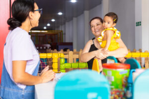 Two adult women and a baby sharing a welcoming moment at a childcare center, reflecting trust, care and family support, Latina women and baby 1 to 2 years