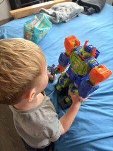 A three-year-old playing with a robot toy on his bed