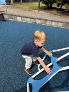 A three-year-old boy in a blue shirt climbing on a playground structure