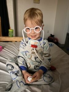 A three-year-old boy wearing glasses and a stethoscope playing